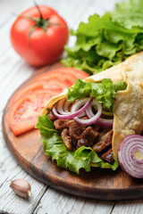 Doner kebab is lying on the cutting board. Shawarma with meat, onions, salad lies on a white old wooden table.
