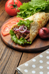Doner kebab is lying on the cutting board. Shawarma with meat, onions, salad lies on a dark old wooden table.