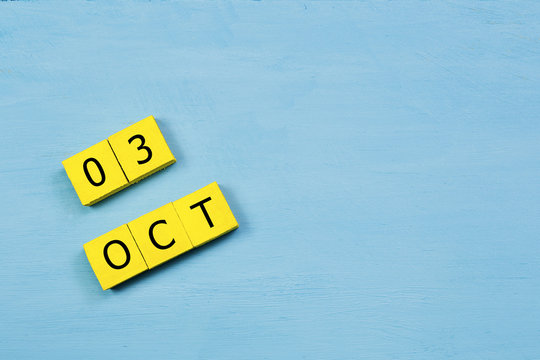 OCT 3, yellow cube calendar on blue wooden surface with copy space