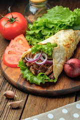Doner kebab is lying on the cutting board. Shawarma with meat, onions, salad lies on a dark old wooden table.