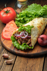 Doner kebab is lying on the cutting board. Shawarma with meat, onions, salad lies on a dark old wooden table.