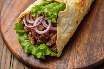 Doner kebab is lying on the cutting board. Shawarma with meat, onions, salad lies on a dark old wooden table.