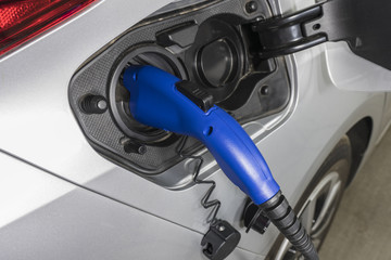 Close up of electric vehicle plug charging car inside garage.  