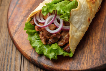 Doner kebab is lying on the cutting board. Shawarma with meat, onions, salad lies on a dark old wooden table.