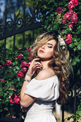 Outdoor portrait of young beautiful curly girl near forged lattice with roses.
