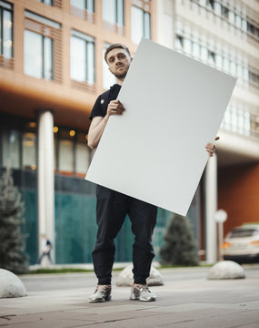Attractive man holding blank canvas at the street and looking at the viewer.