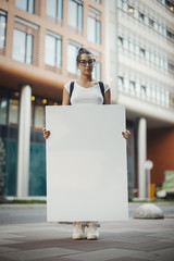 Young Intelligent Attractive Woman Holding Blank Canvas Placard Outdoors. Activist Protesting Against Political and Social Issues. Copy Space. Empty Space. Single Person Protest In The City