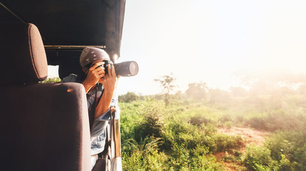 Woman photographer takes a picture with professional camera from touristic vehicle on tropical safari - obrazy, fototapety, plakaty
