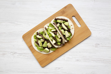 Tortillas with grilled beef, avocado on the bamboo board over white wooden surface. View from above, overhead, flat-lay.