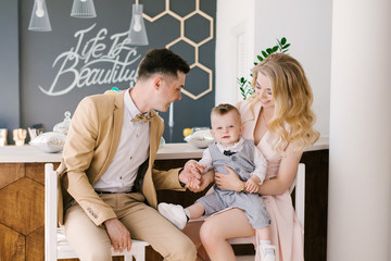 Beautiful young parents smile with their one-year-old child at home in a beautiful interior in pastel colors. Family look. Happy birthday party