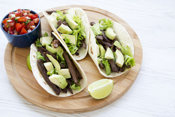 Tacos with salsa on the bamboo board on a white wooden background, side view. Mexican kitchen.