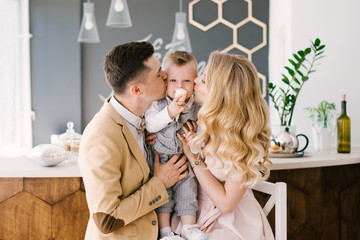 Beautiful young parents kiss their year-old child at home in a beautiful interior in pastel colors. Family look. happy birthday