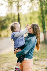Fototapeta premium Happy smiling mother hugging her lovely little daughter outdoor. Lifestyle family. Adult cheerful female parent playing with her beautiful emotional child at nature in summer. Positive people faces.
