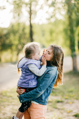 Fototapeta premium Happy smiling mother hugging her lovely little daughter outdoor. Lifestyle family. Adult cheerful female parent playing with her beautiful emotional child at nature in summer. Positive people faces.