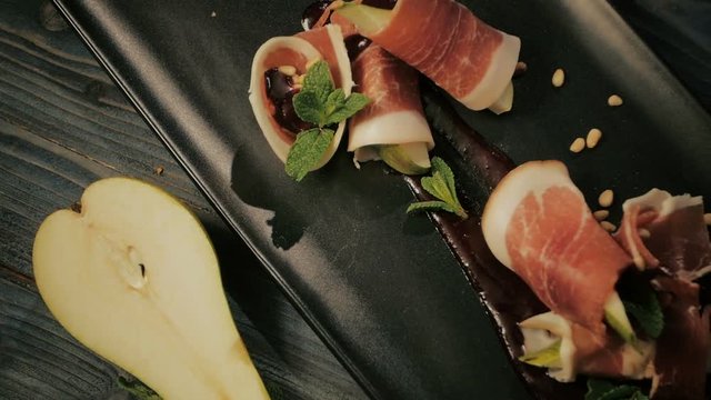 Prosciutto with pear and berry sauce. Cold snacks. dolly shot. On a black wooden background.