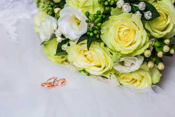 Wedding gold rings near bouquet of roses on wedding white dress