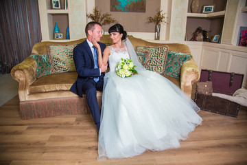 Bride in white dress, stroking groom's chin and looking at him, in luxurious room