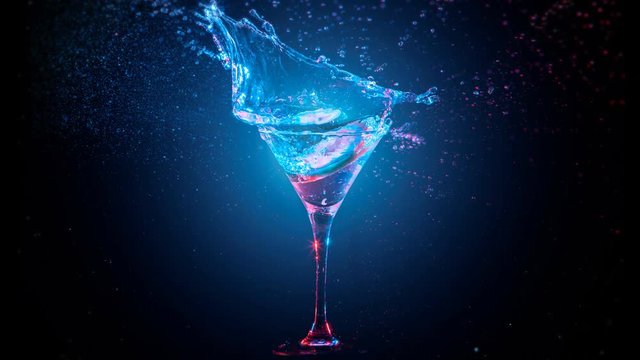 Bright modern cocktail with lemon falling in glass, splashing water on dark background. Blue and red color mixed light. Drops, bokeh and glare moves on the frame. Frozen in motion. Slow motion 4K