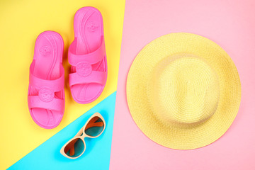 Hat, sunglasses and slippers on a three-color pastel background of blue, yellow and pink.