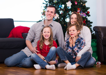 smiling parents and children posing for photo by Christmas tree