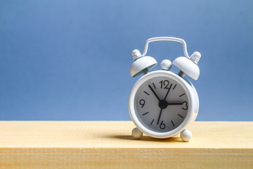 White small alarm clock on a wooden shelf on a grey pastel background. Minimalism.
