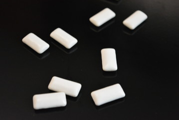 On a black glossy background, white pillows from chewing gum are laid and lie, health and caring...