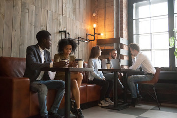 Multiracial people sitting in coffee shop, enjoying morning coffee, using gadgets working, checking...