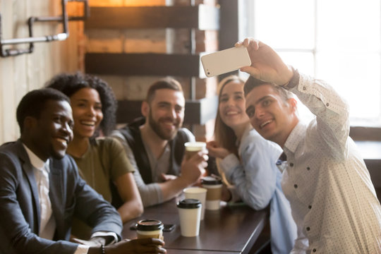 Millennial multiracial friends smiling posing for camera, taking self-portrait on smartphone while enjoying coffee in cafe, young people making selfie on mobile phone at meeting in coffee shop.