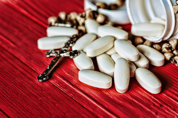 silver Christian cross necklace white pills on red wooden, religious concept 