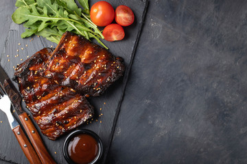 Closeup of pork ribs grilled with BBQ sauce and arugula. Tasty snack to beer on a stone Board for...