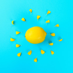 Yellow whole lemon in the form of the sun and rays from the petals of a yellow flower on a pastel blue background.