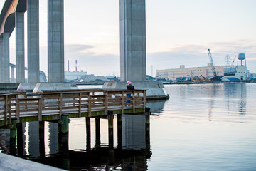 A little girl in a pink hat stands on a pier and looks out thoughtfully into the water of the...