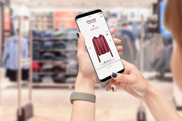 Girl searching for clothes with smartphone, clothing store in background