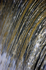 Water cascade waterfall streaming torrent splashes background large detailed vertical closeup, bright blue, golden, yellow sea green pastel colors motion blurred drops texture pattern textured bokeh