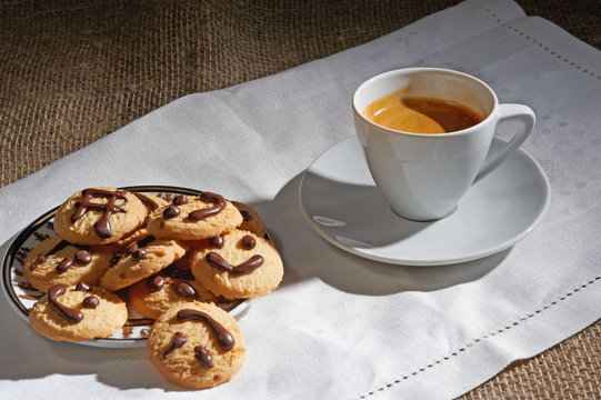 A cup of black coffee and biscuits on white napkin
