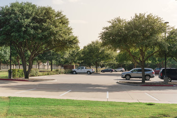 Cars parked under the tree shade at large public parking in Coppell, Texas, USA.