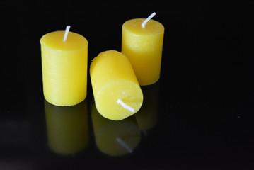 On a black glossy background there are beautiful three round yellow candles with reflection