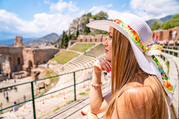 Jule 04, 2018. Taormina, Italy. Beautiful girl in a long white dress and white summer hat sitting...