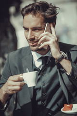 Young handsome business man having his espresso coffee and talking on his cell phone