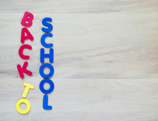 colorful foam letters spelling the words Back to School in vertical rows on a wooden desk with copy...