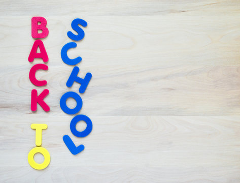 colorful foam letters spelling the words Back to School in vertical rows on a wooden desk with copy space