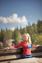 Naklejka na ściany i meble Young blonde woman, a traveller, enjoying an outdoor view of tall mountains landscape from a balcony viewpoint