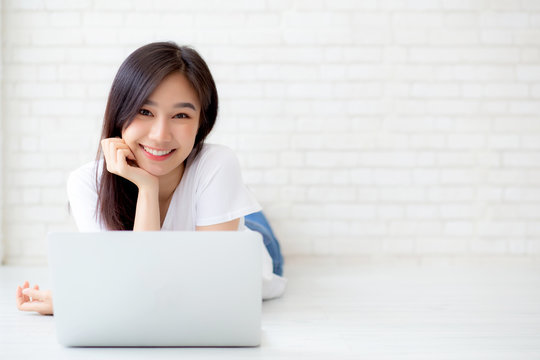 Beautiful portrait asian woman working online laptop lying on floor brick cement background, freelance girl using notebook computer with connect to internet for job, business and lifestyle concept.