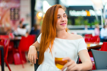 Young redhead pretty girl enjoying a beer at a mall