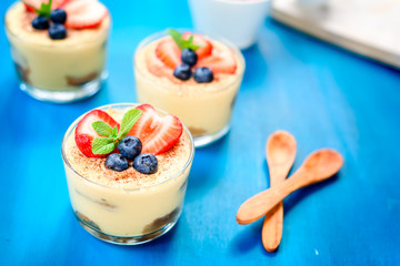 homemade, exquisite dessert tiramisu in glasses decorated with strawberry, blueberry, mint on blue wooden table