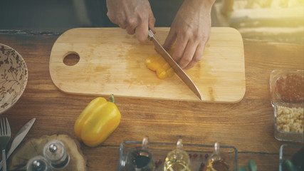 A closeup of male hands cutting slicing a yellow paprika on a wooden kitchen cooking board olive and ingredients surrounding