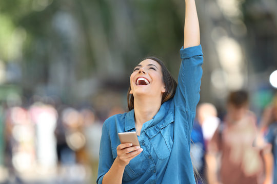 Excited woman holding phone and raising arm