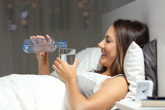 Woman throwing water in a glass from a bottle in the bed
