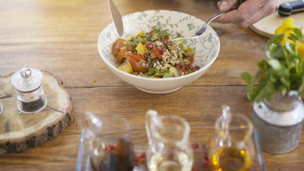 A knife and a fork held above ready green fresh salad of cucumbers, tomatoes, paprika seeds in a bowl plate on a kitchen table