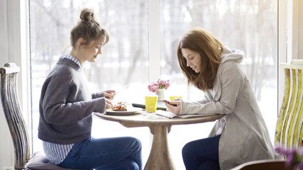 Two female friends sitting in a cafe face to face preparing for the exam talking making notes eating salad